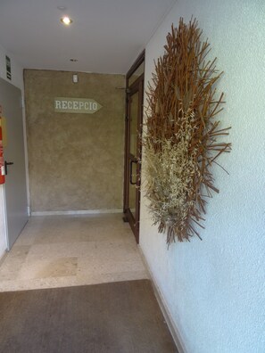 A reception area with a sign labeled "RECEPCIO" on the wall, a door, and a decorative plant on the wall. - Aparthotel Sant Andreu (Arinsal)