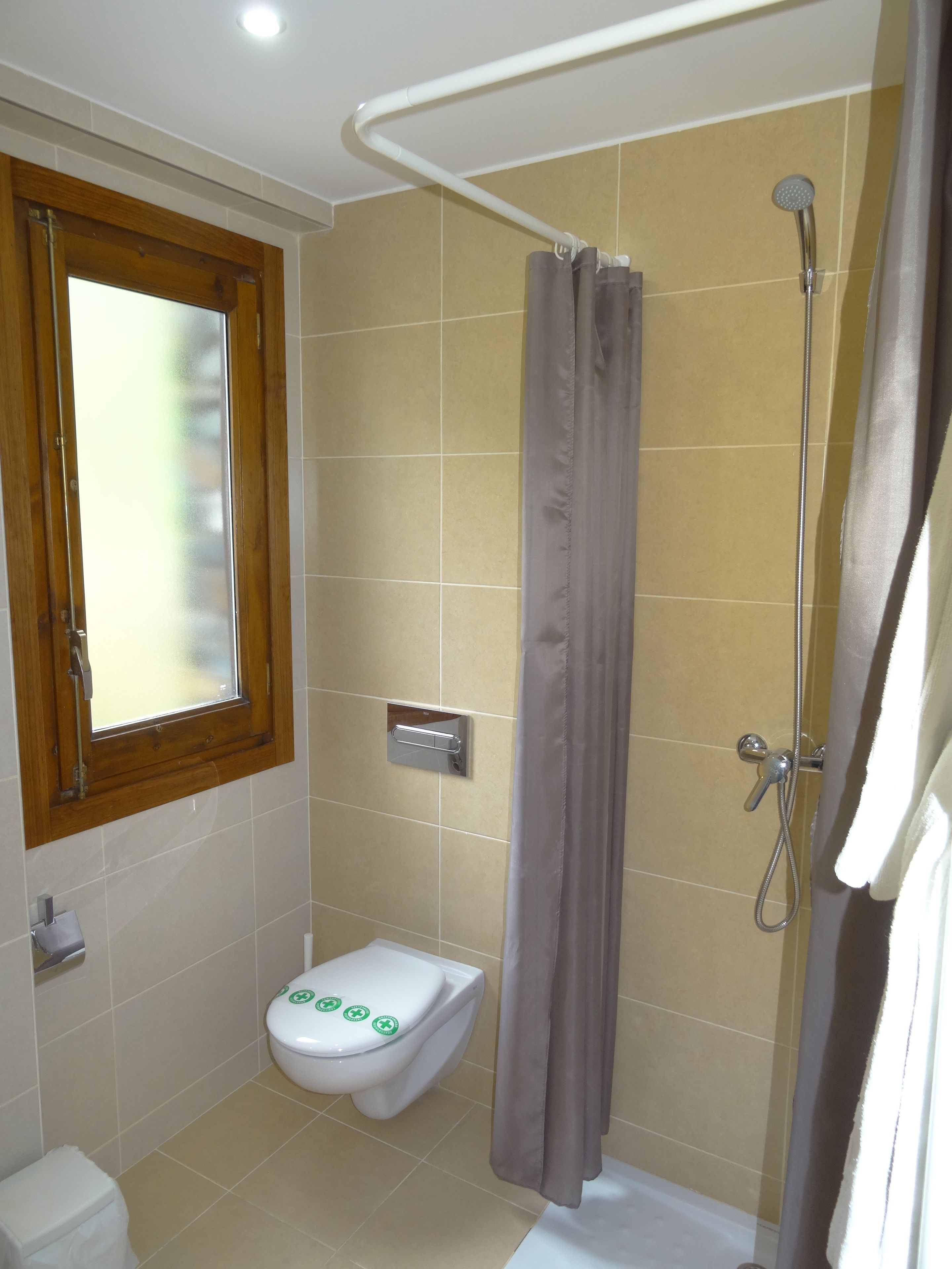 Een kleine badkamer met toilet, douche en raam.