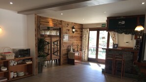 Hall d'albergo con reception in legno, angolo buffet e vista sulla zona salottino all'aperto.