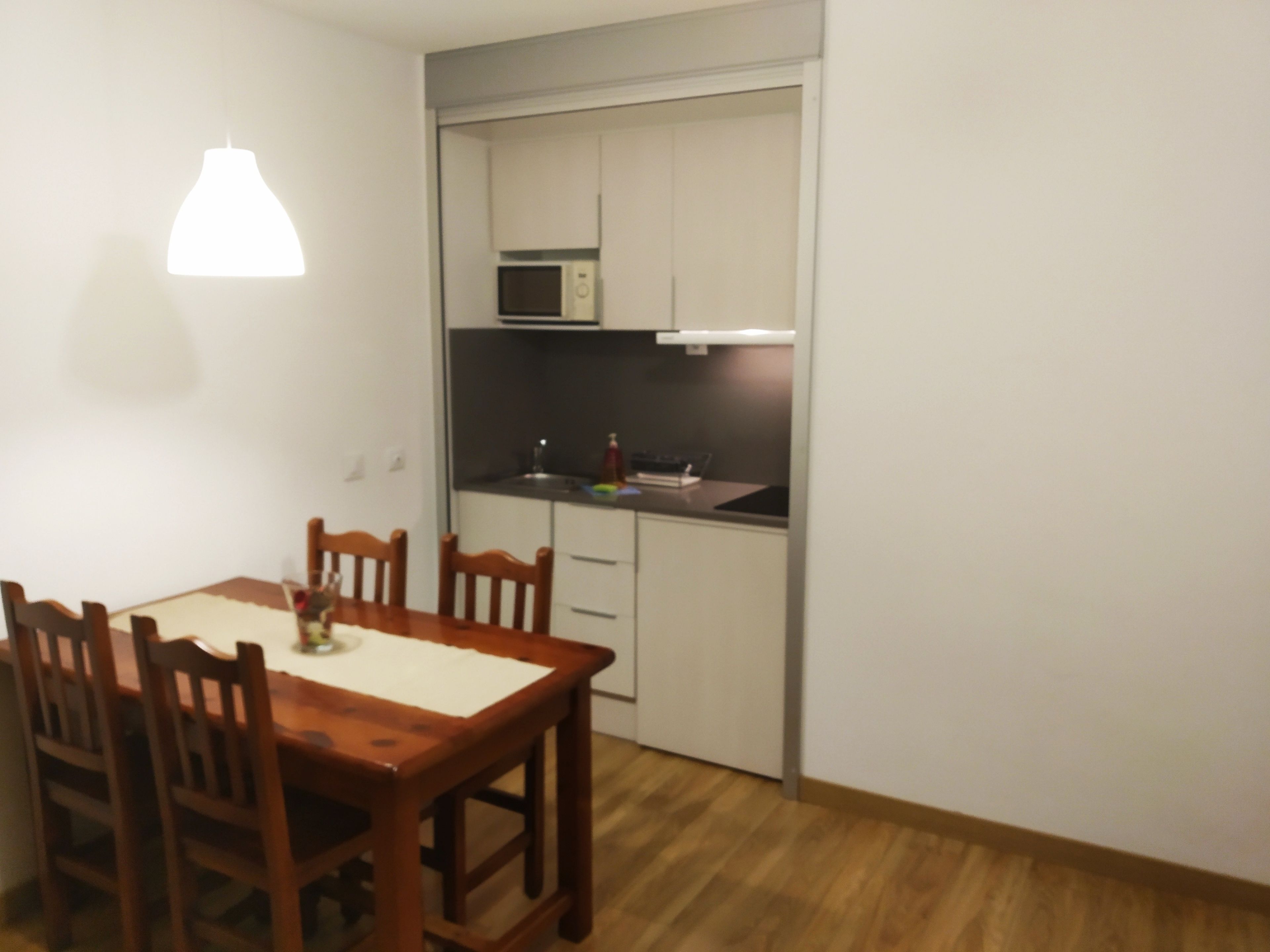 A compact kitchen with white cabinets, a microwave, and a dining table with chairs.