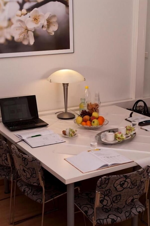 Una mesa de comedor con una computadora portátil, un cuenco de fruta, una lámpara y un cuadro en la pared.