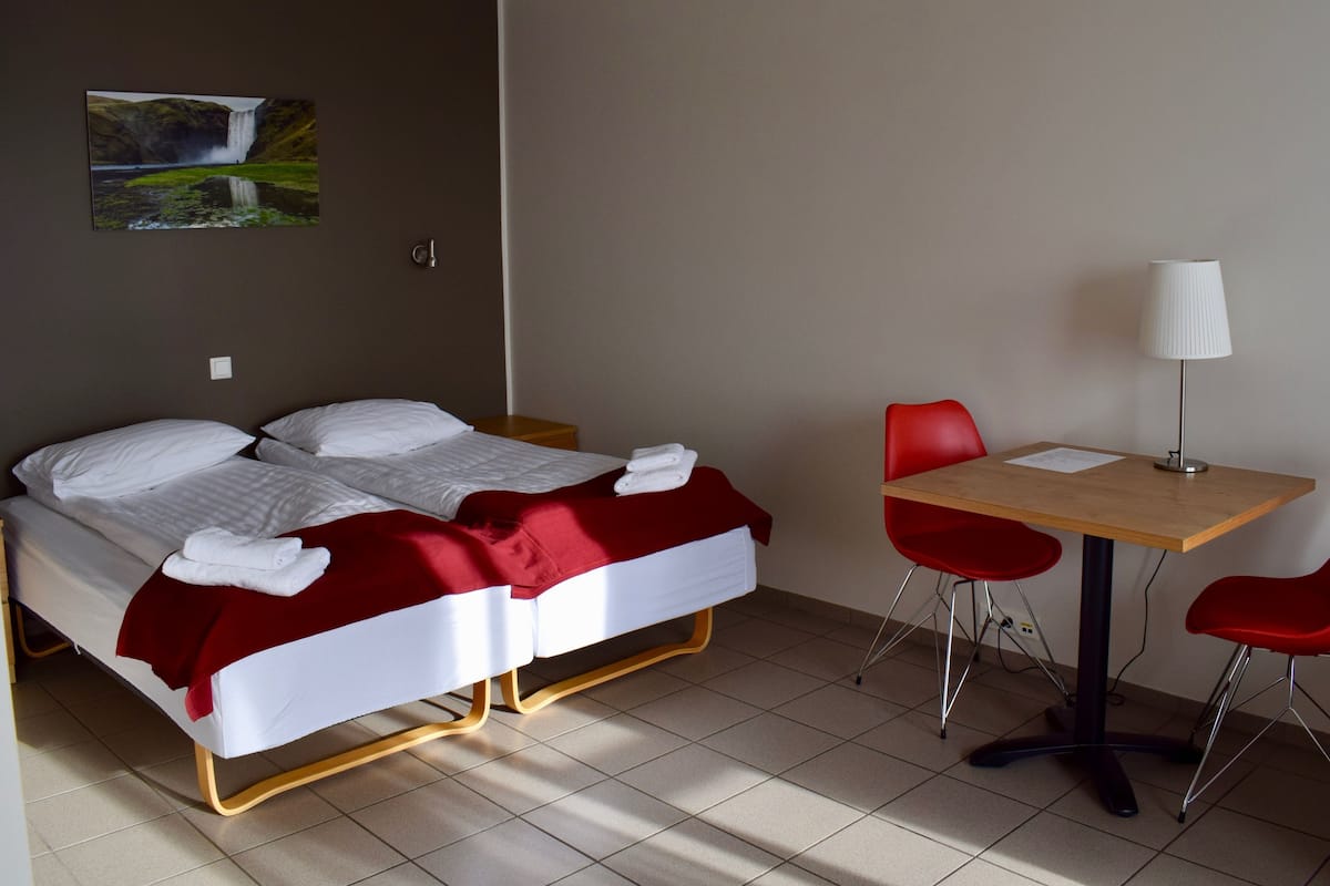 Egy szállodai szoba két ággyal, íróasztallal és két piros székkel.