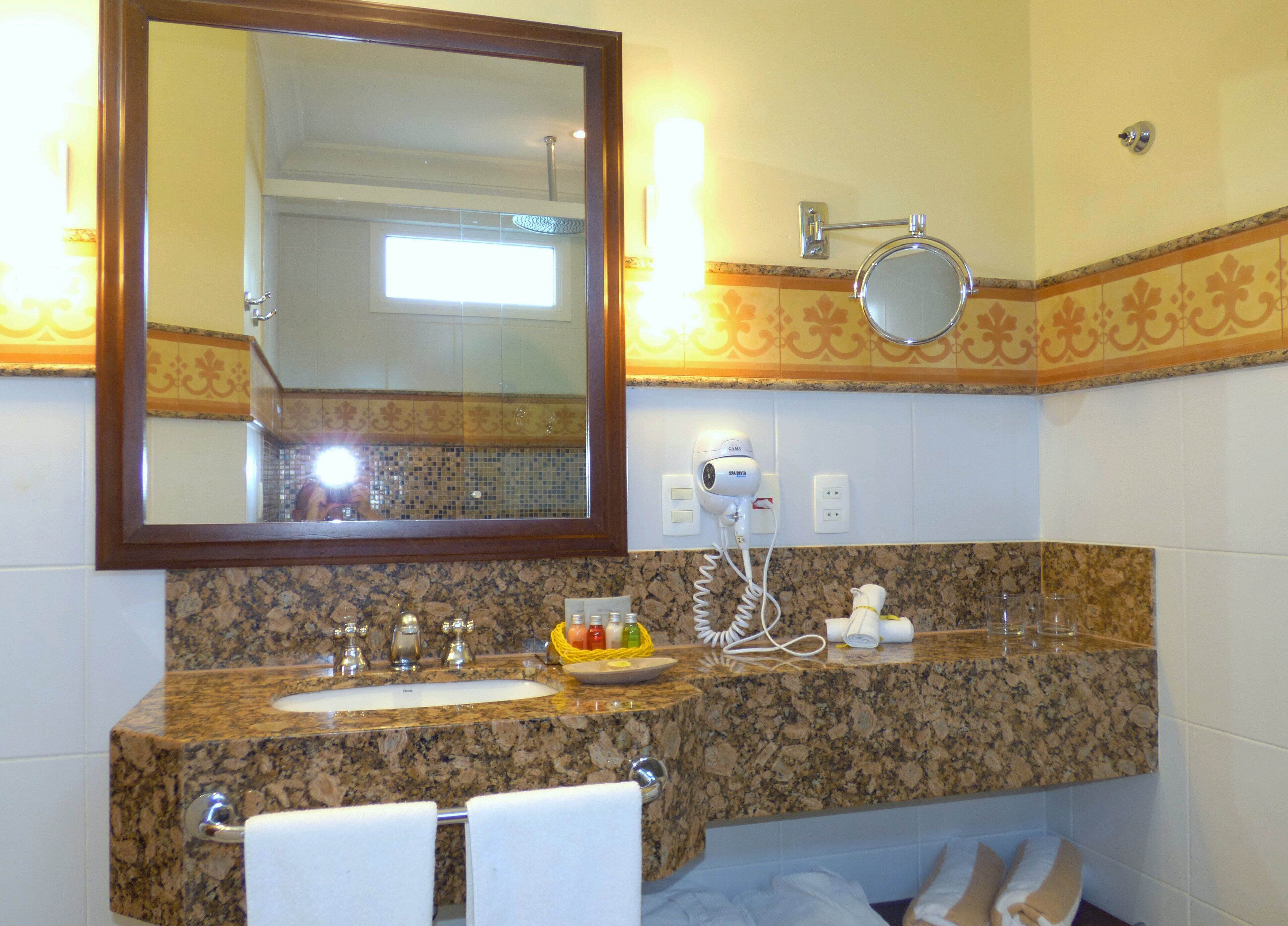 Un baño con encimera de granito, lavamanos, espejo, secador de pelo y toallero.