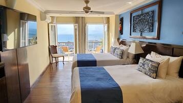 A hotel room with two beds, a balcony with a view, a ceiling fan, and a large window.