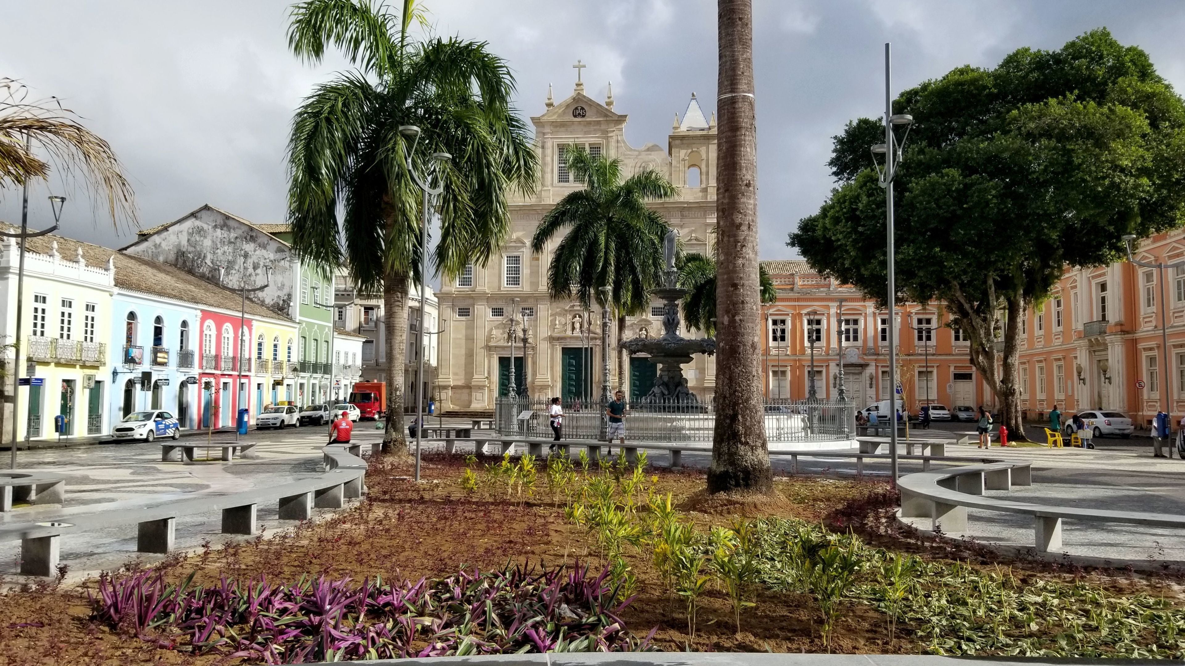 Una plaza con una fuente central, rodeada de palmeras y edificios de colores.
