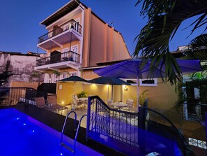 Una piscina con barandilla metálica, rodeada de mobiliario exterior y sombrillas.