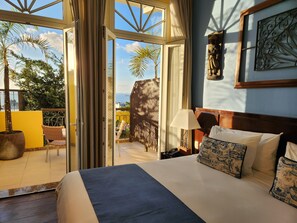 A hotel room with a large bed, a view of the sea, and a balcony with outdoor furniture. - Casa do Amarelindo (Salvador)