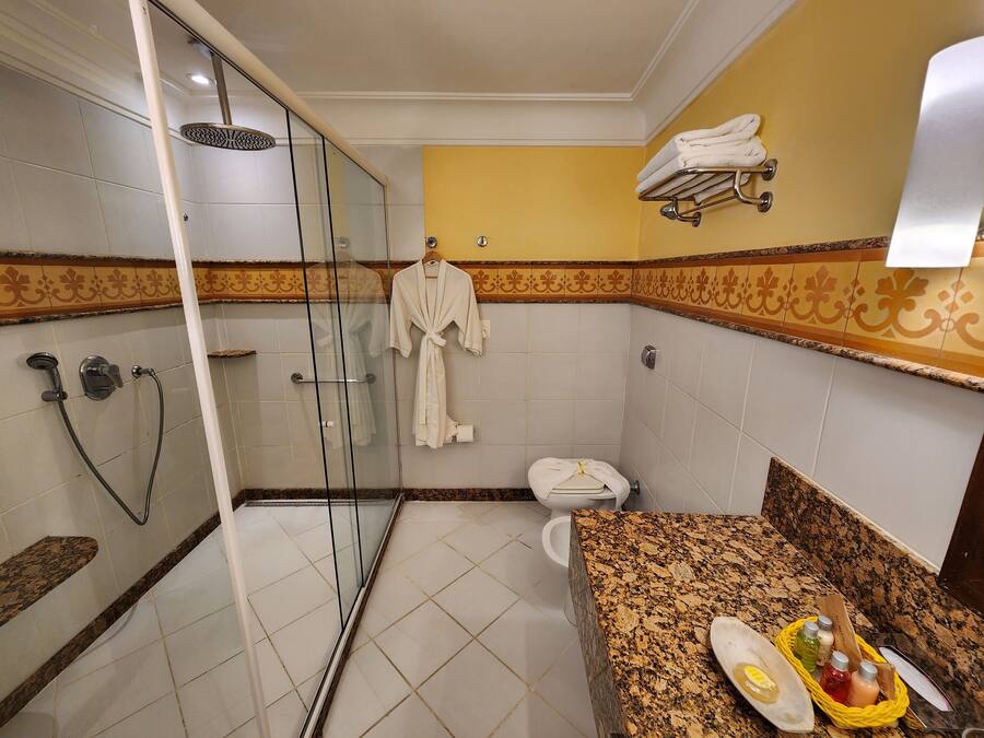 Un baño con cabina de ducha de vidrio, inodoro, lavamanos con encimera de granito y toallero con toallas.