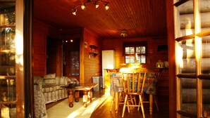 Interior acogedor de una cabaña con una mesa de comedor de madera, sillas, sofá y un refrigerador.