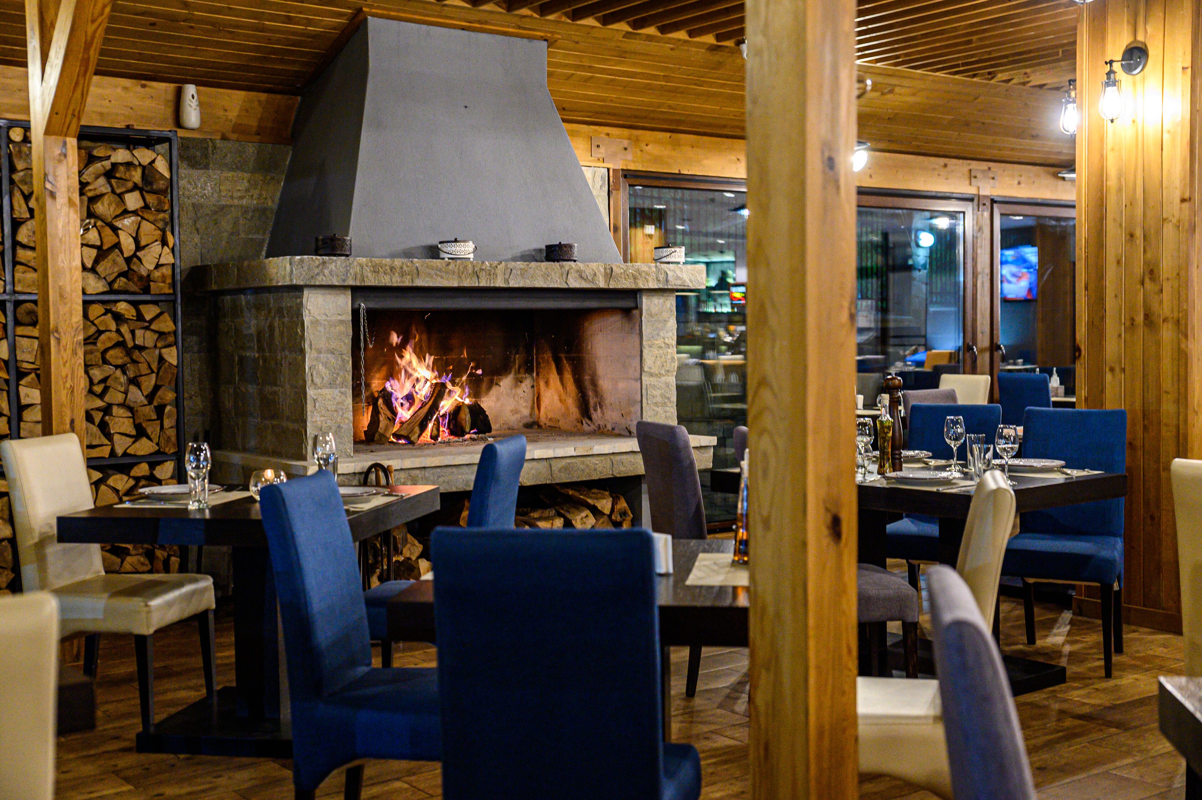 A restaurant with a stone fireplace, wooden beams, and blue upholstered chairs.