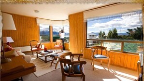 Un salon chaleureux avec un lambris en bois, un canapé, une table basse et une vue sur un paysage montagneux grâce à de grandes fenêtres.