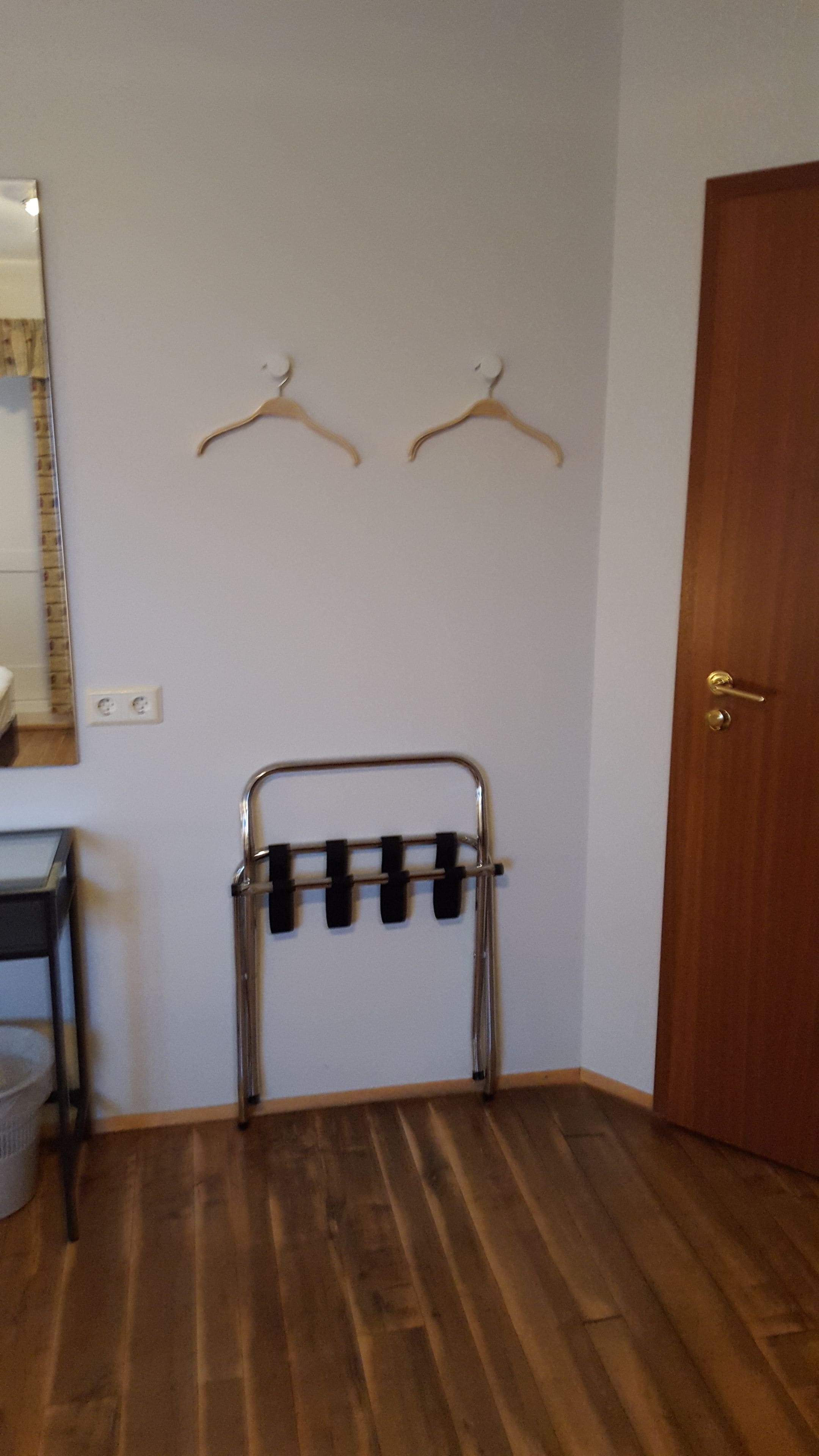 Una habitación con piso de madera, una puerta, un espejo y dos colgadores de madera en la pared.