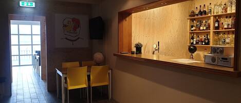 A bar area with wooden shelves stocked with bottles, a counter with a cash register, and yellow chairs.