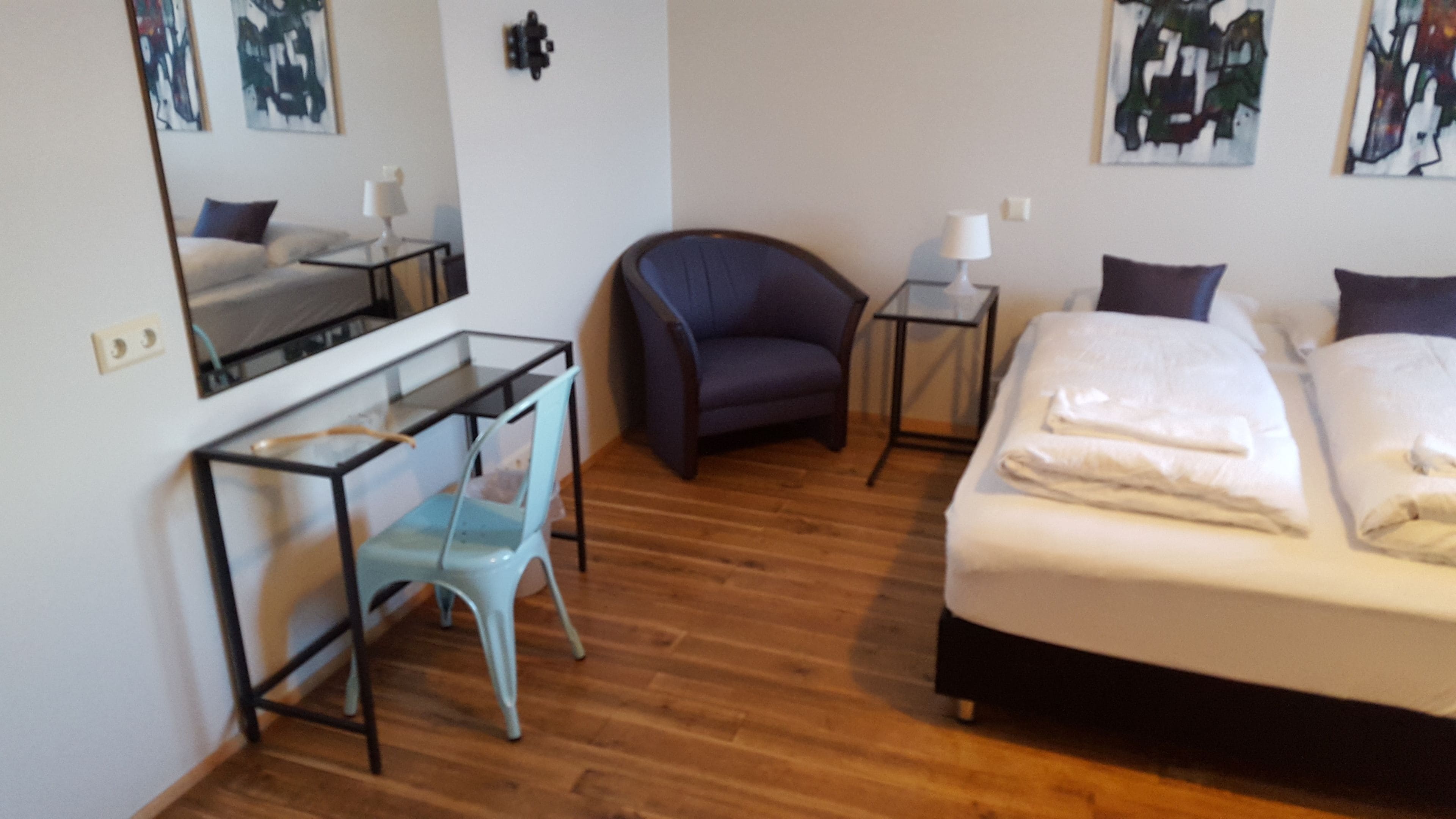 Ein Hotelzimmer mit Bett, Schreibtisch mit Stuhl, kleinem Tisch und einem weiteren Stuhl.