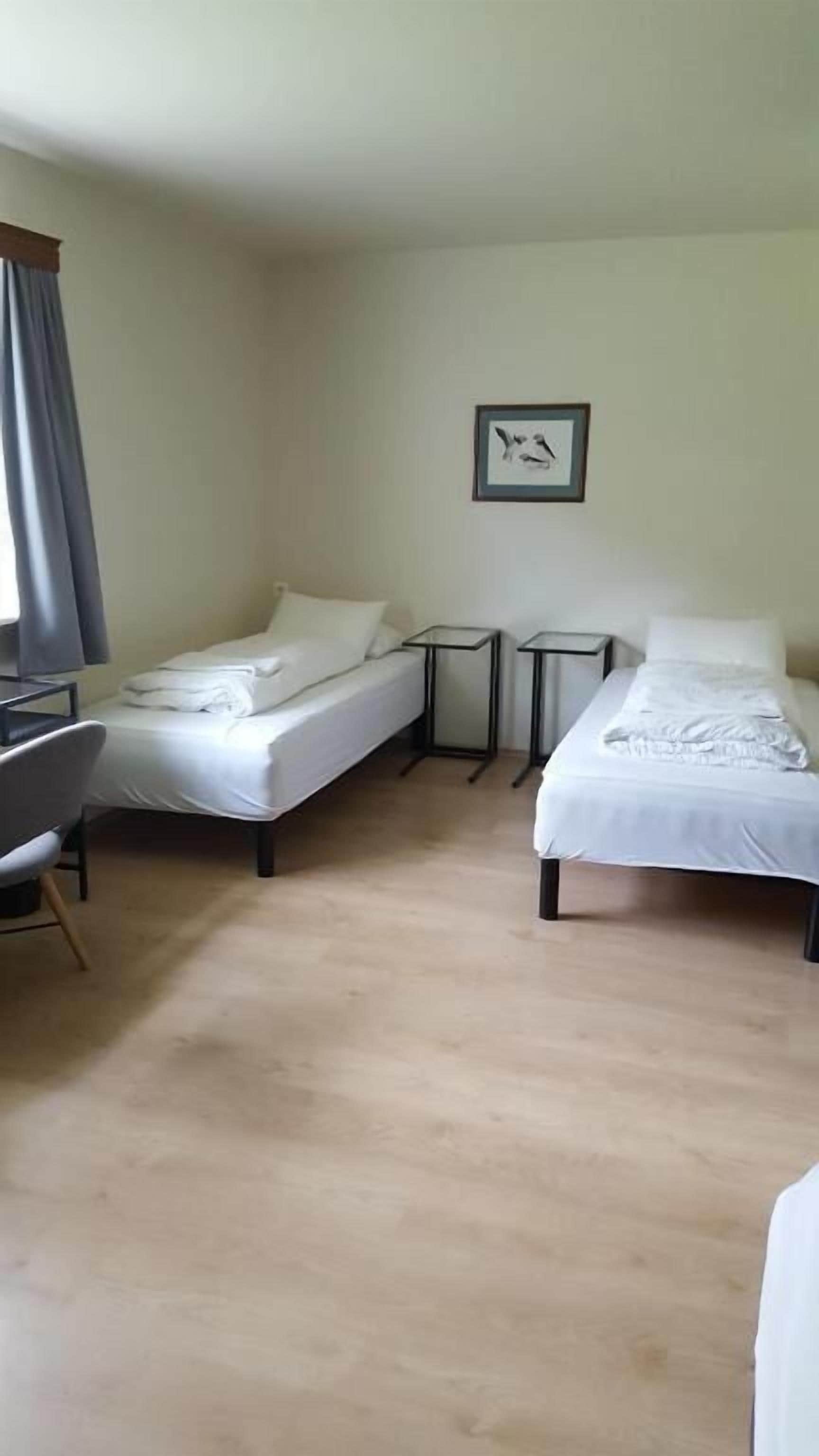 A room with two beds, a desk, and a chair. There is a framed picture on the wall.