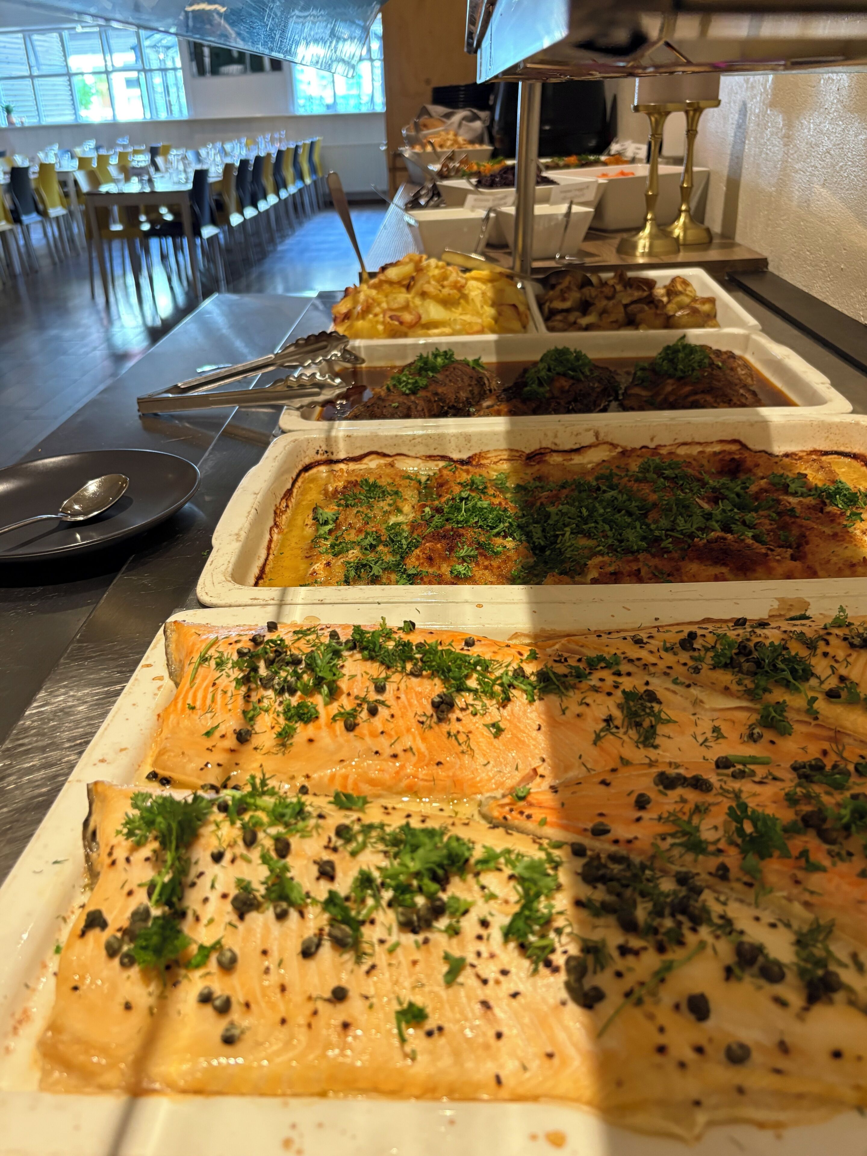 Um buffet com diversos pratos, incluindo salmão, legumes e outros alimentos já preparados.