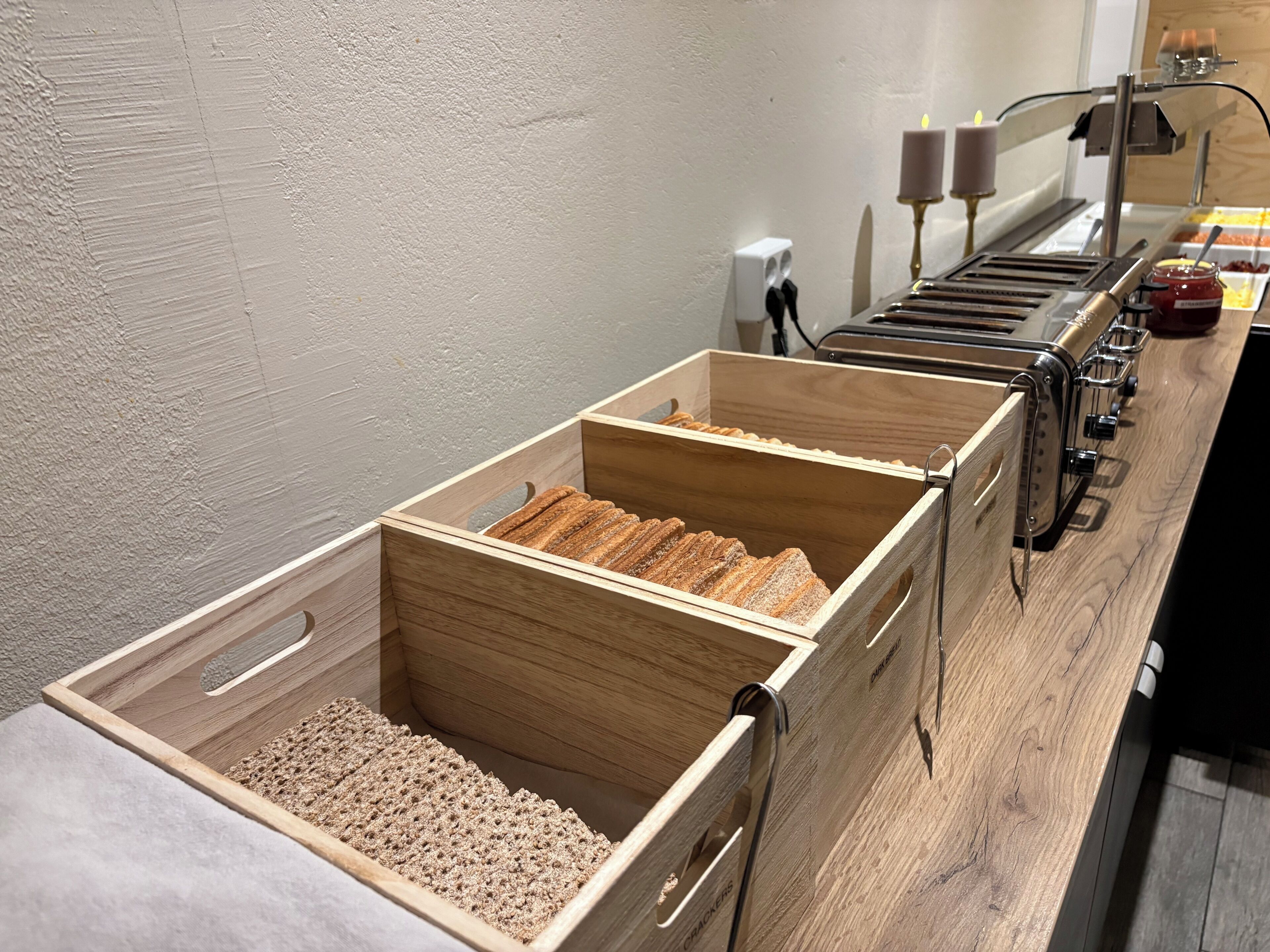 A buffet setup with wooden serving trays and a candle on the wall.