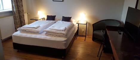 A hotel room with a bed, two bedside lamps, a chair, a desk, and a television.