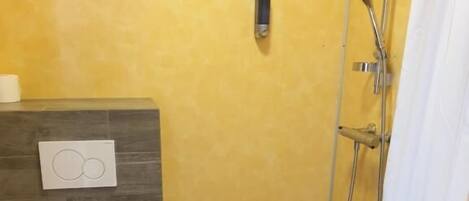 Une petite salle de bain avec des toilettes, une douche et une serviette accrochée au mur.