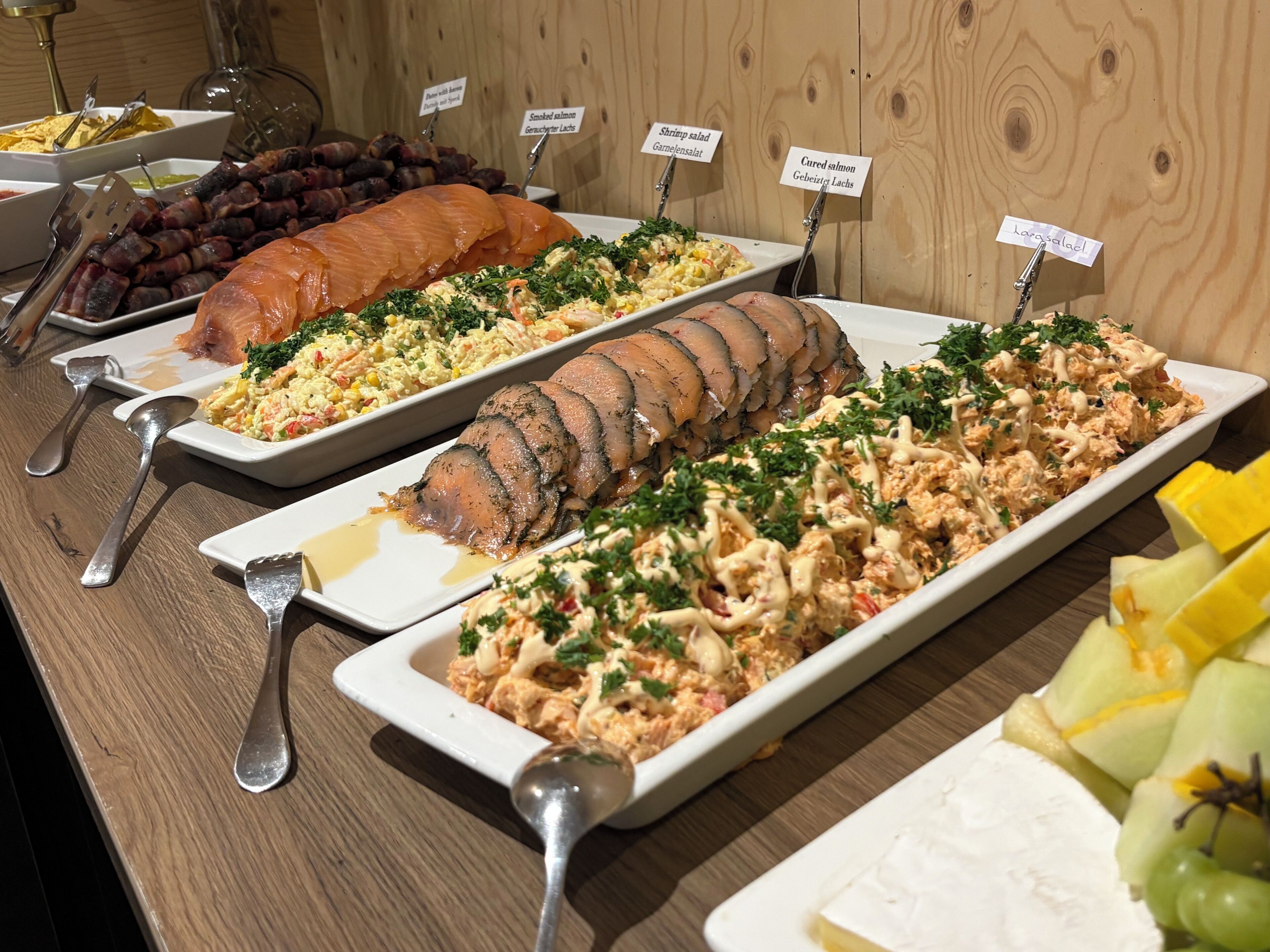 A buffet table with various dishes including smoked salmon, shrimp salad, and cured salmon.
