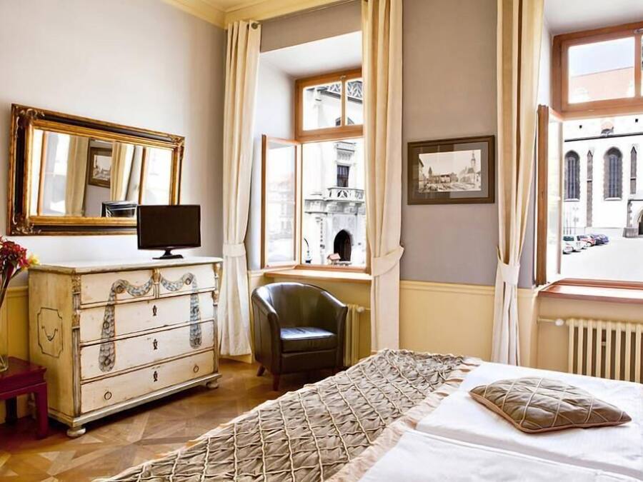A hotel room with a bed, a dresser, a chair, a TV, and a window with a view of a building.