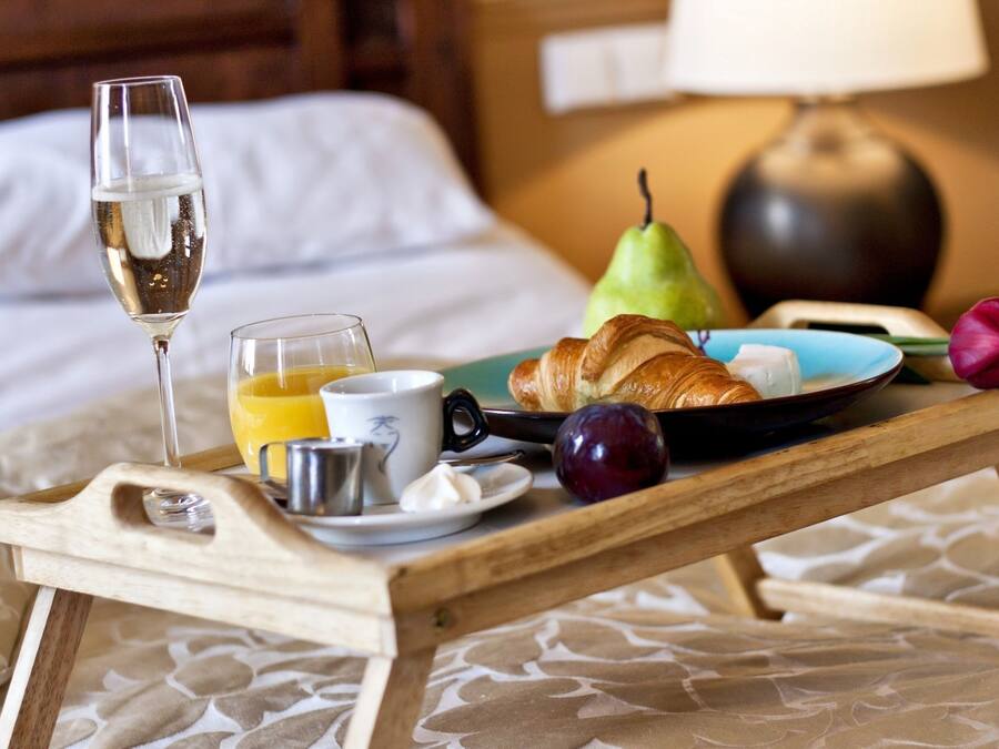Bandeja de café da manhã com croissants, uma pera, ameixa, copo de suco de laranja, xícara de café e taça de champanhe sobre a cama.