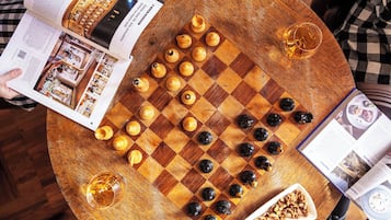 Un jeu d’échecs est posé sur une table ronde en bois, à côté d’un magazine et d’un bol de noix.