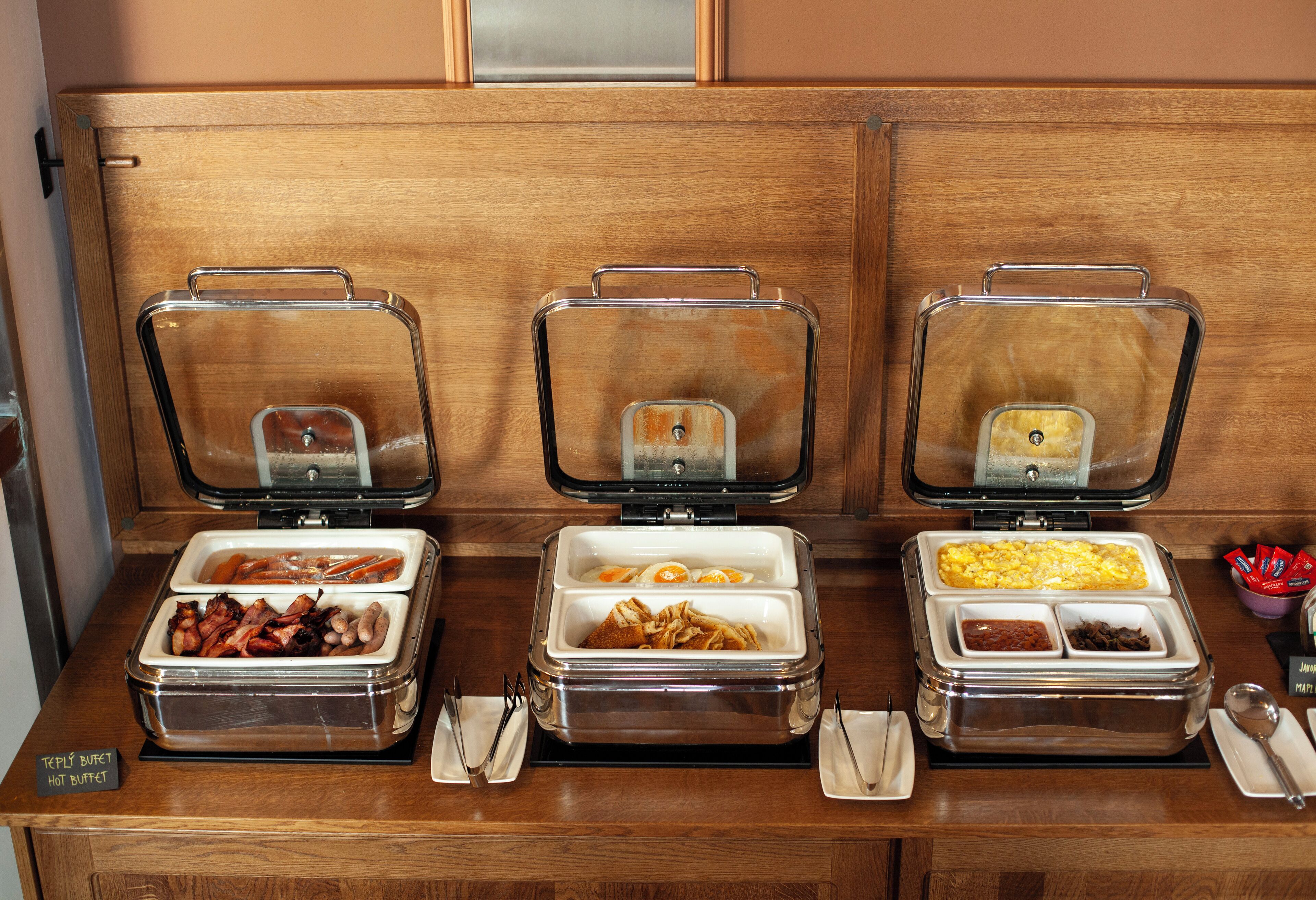 A buffet setup with various food items in clear containers, including meats, eggs, and other breakfast foods.