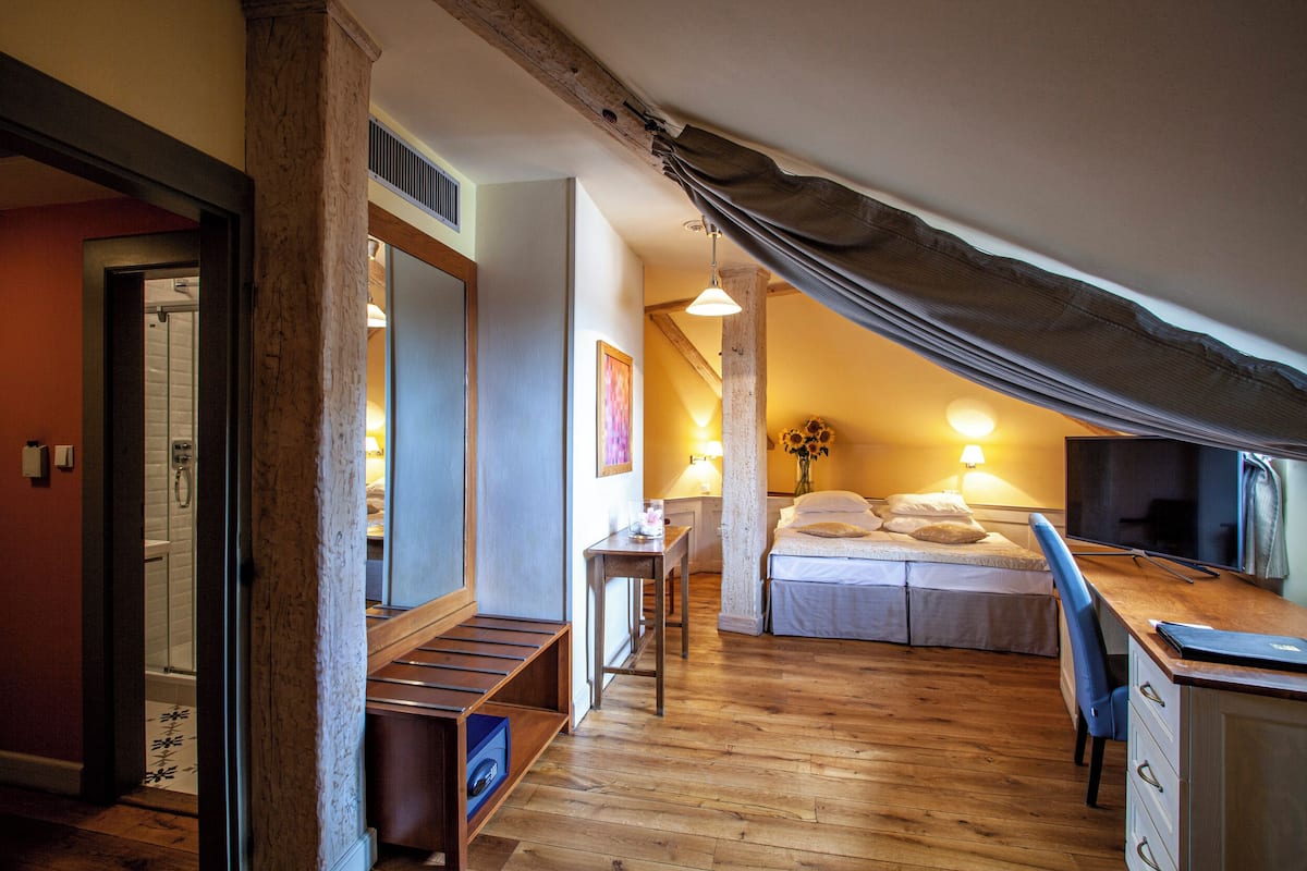 A bedroom with a wooden floor, a desk, a chair, a bed, and a window with curtains.