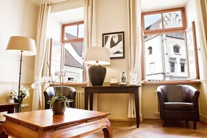 Una habitación con un escritorio de madera, dos sillas, una lámpara, un florero con flores y una ventana con vistas a edificios.