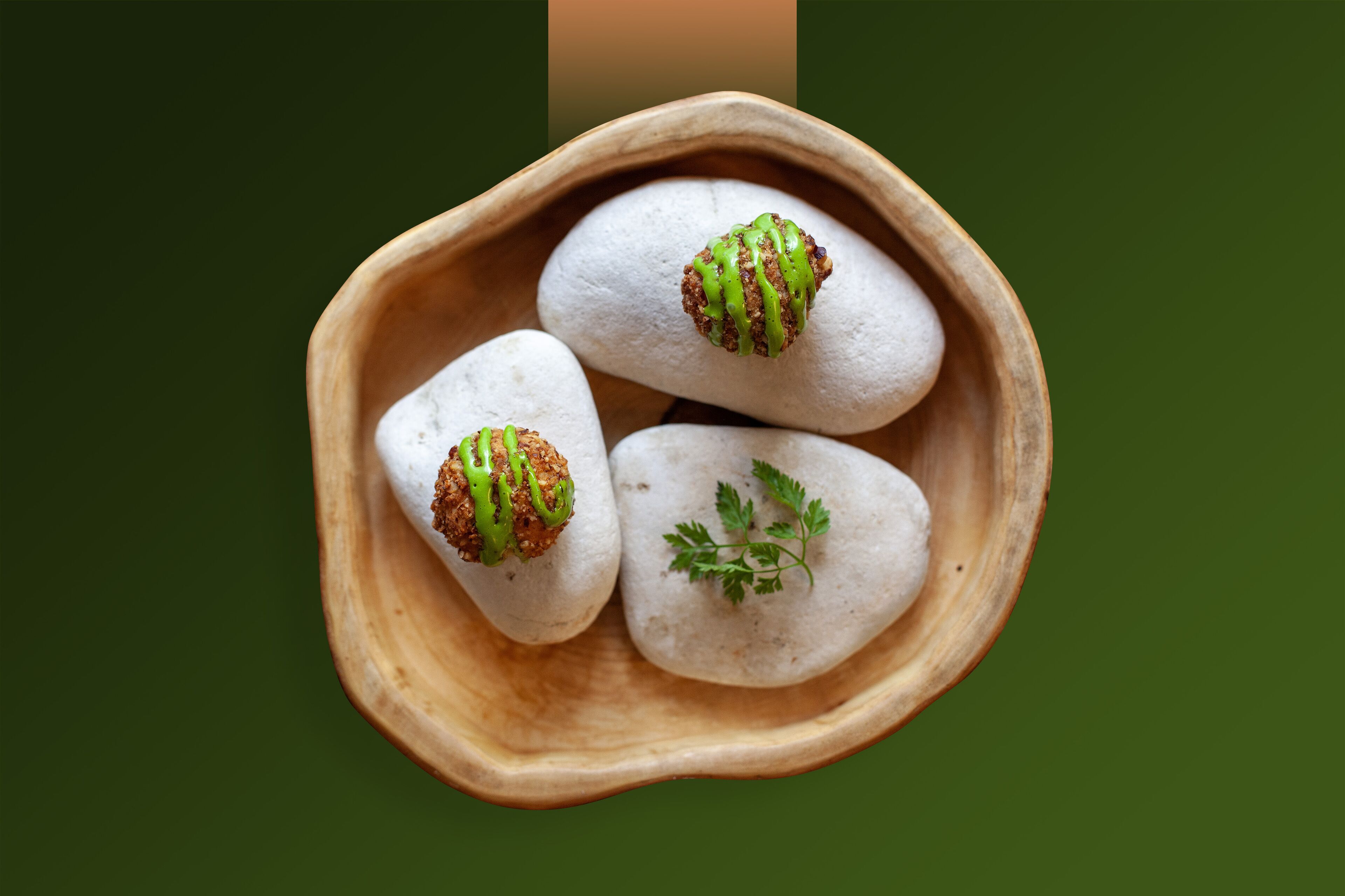 Three white, round objects in a wooden bowl with green and brown drizzles on top.