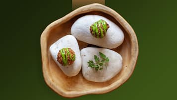Three white, round objects in a wooden bowl with green and brown drizzles on top.