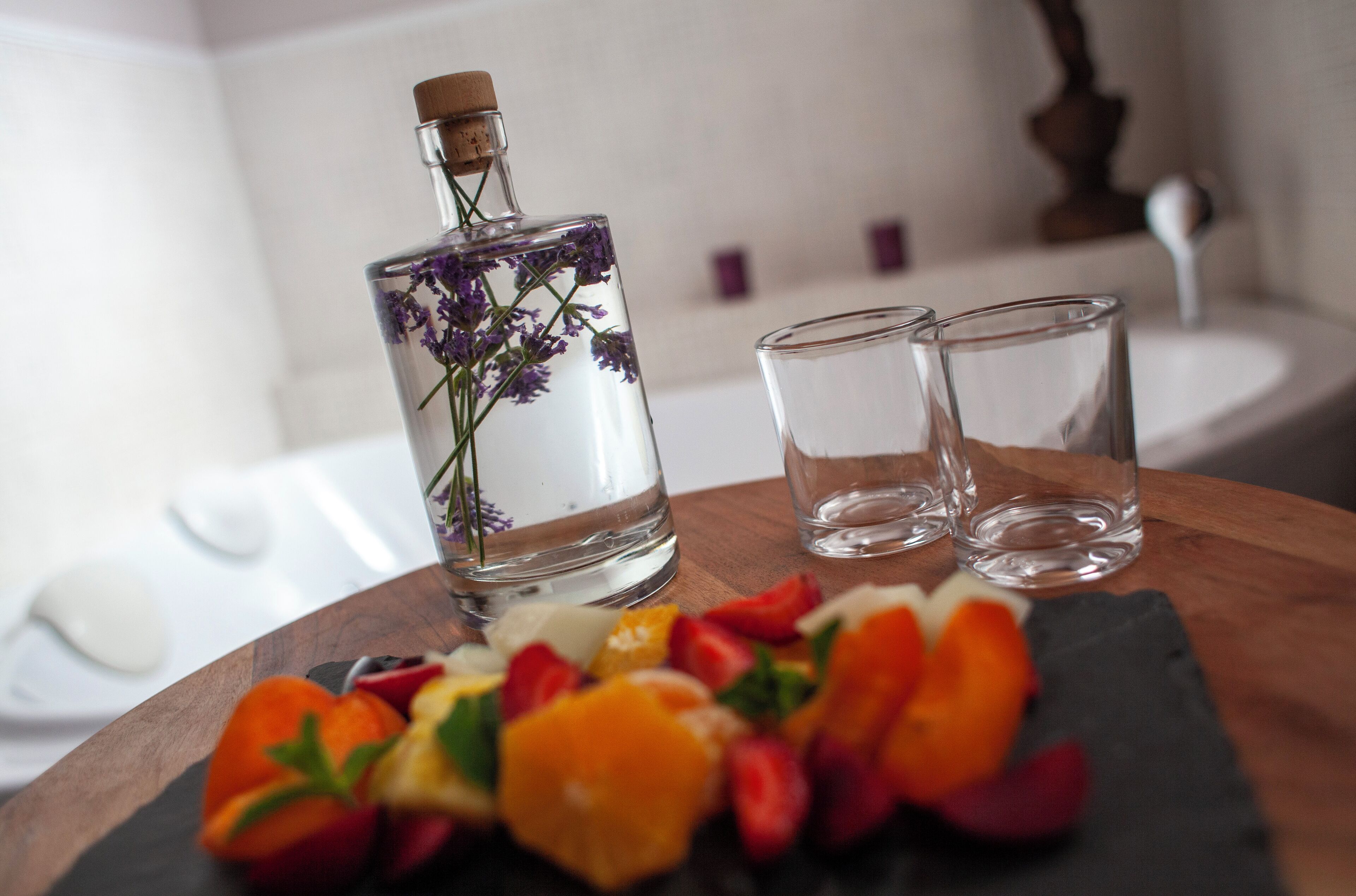 A bottle with lavender flowers, two empty glasses, and a wooden table with fruit slices.