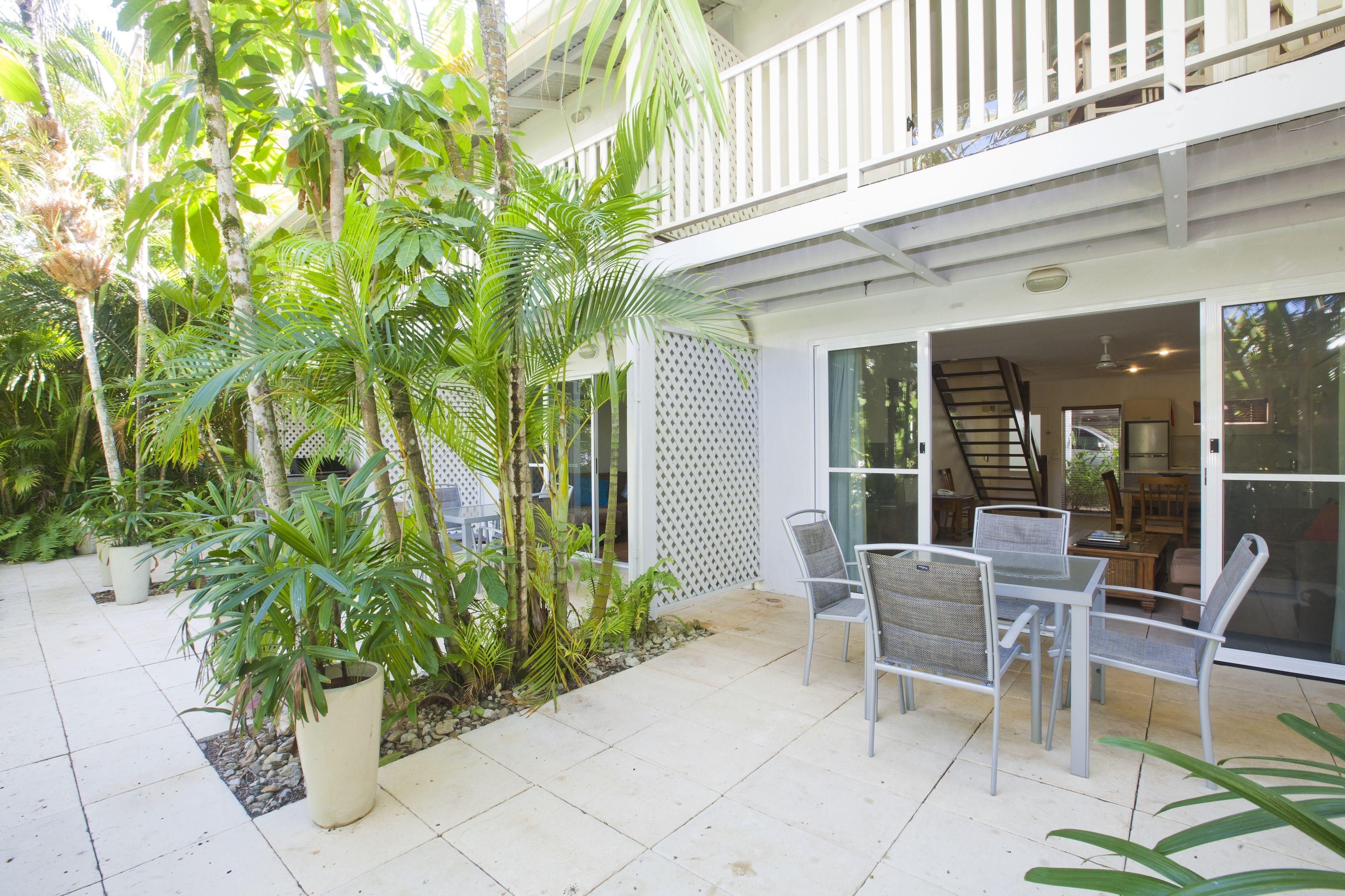 A patio with a table and chairs, surrounded by potted plants and a white fence.