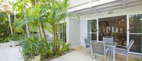 A patio with a table and chairs, surrounded by potted plants and a white fence.