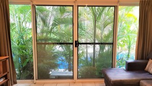 A living room with a sliding glass door leading to a lush garden. - Coral Sea Villas (Port Douglas)