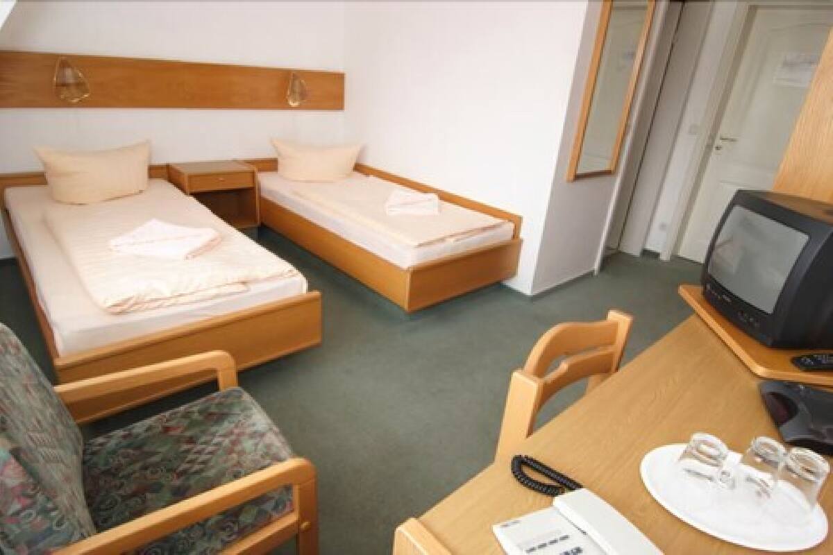 A hotel room with two single beds, a small table with a TV, and a chair.