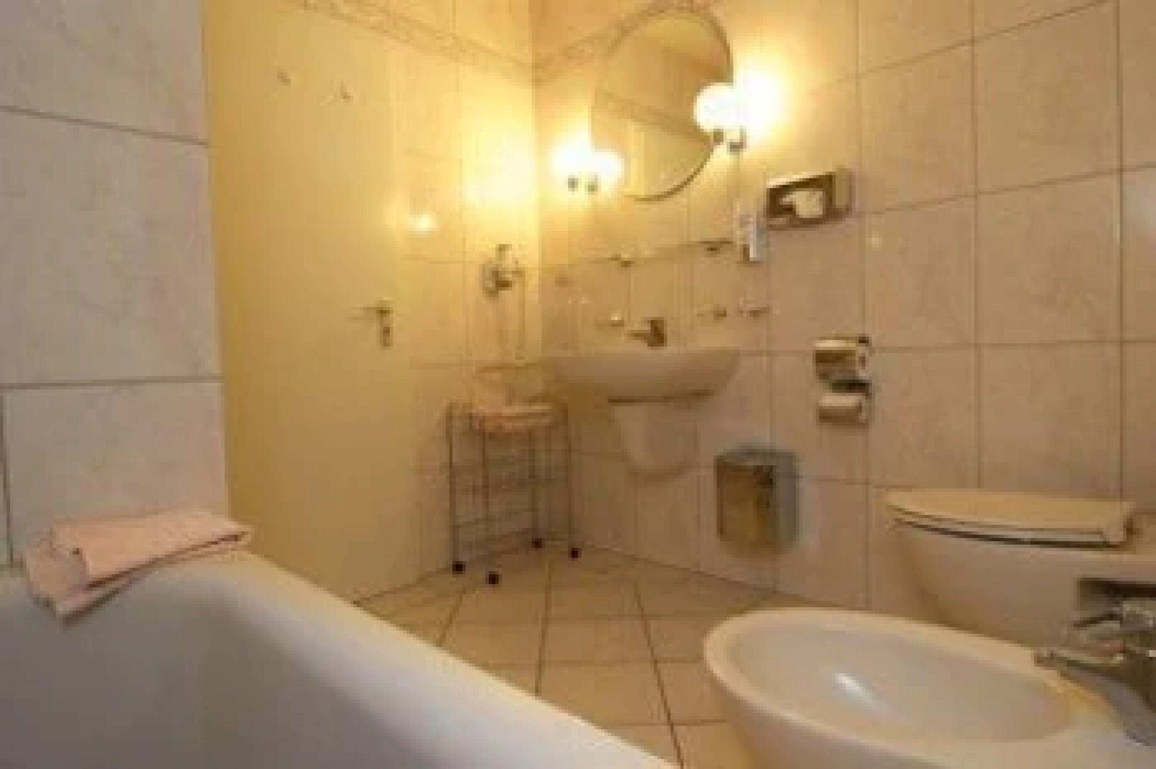 A bathroom with a bathtub, sink, toilet, and a mirror with lights.