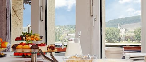 A breakfast buffet with various food items and a milk jug, set against a backdrop of a scenic view through large windows.