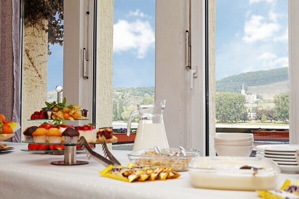 Ein reichhaltiges Frühstücksbuffet mit verschiedenen Speisen und einer Milchkaraffe, vor einer malerischen Aussicht durch große Fenster.
