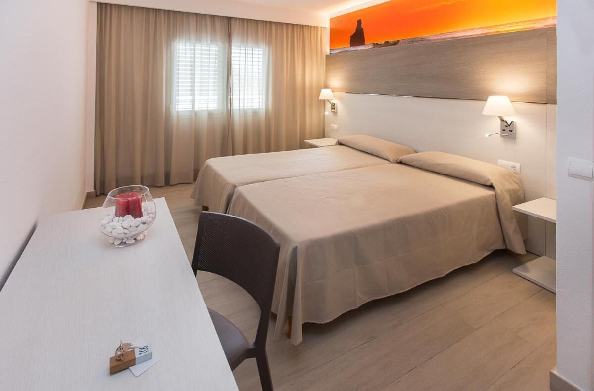 A hotel room with two beds, a table with a candle, and a view of the sunset through the window.