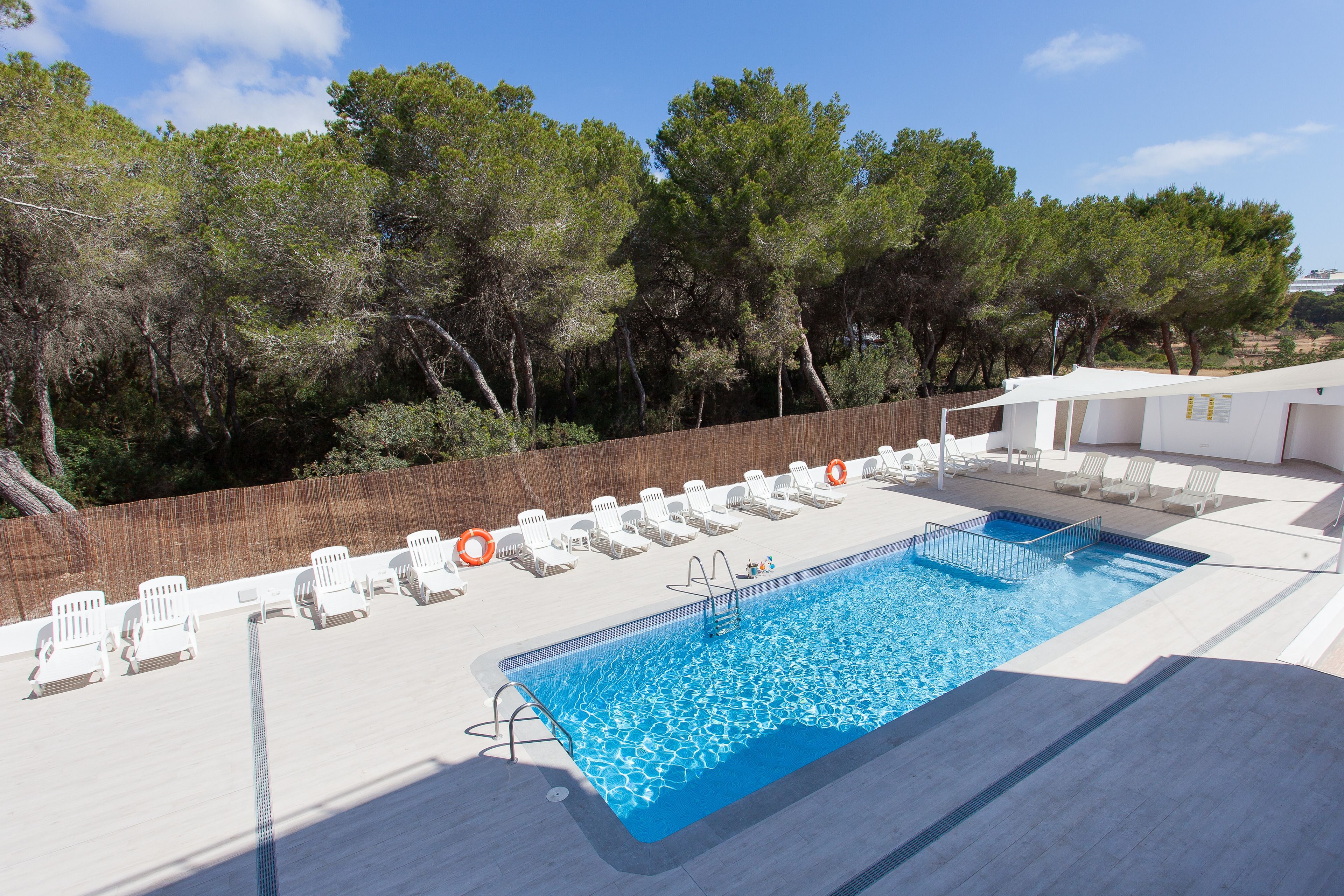 Una piscina con sillas de descanso blancas y una valla de madera.