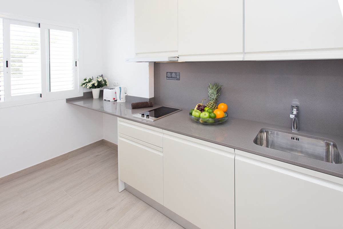 A modern kitchen with a stainless steel sink, a fruit bowl on the counter, and a window with blinds.