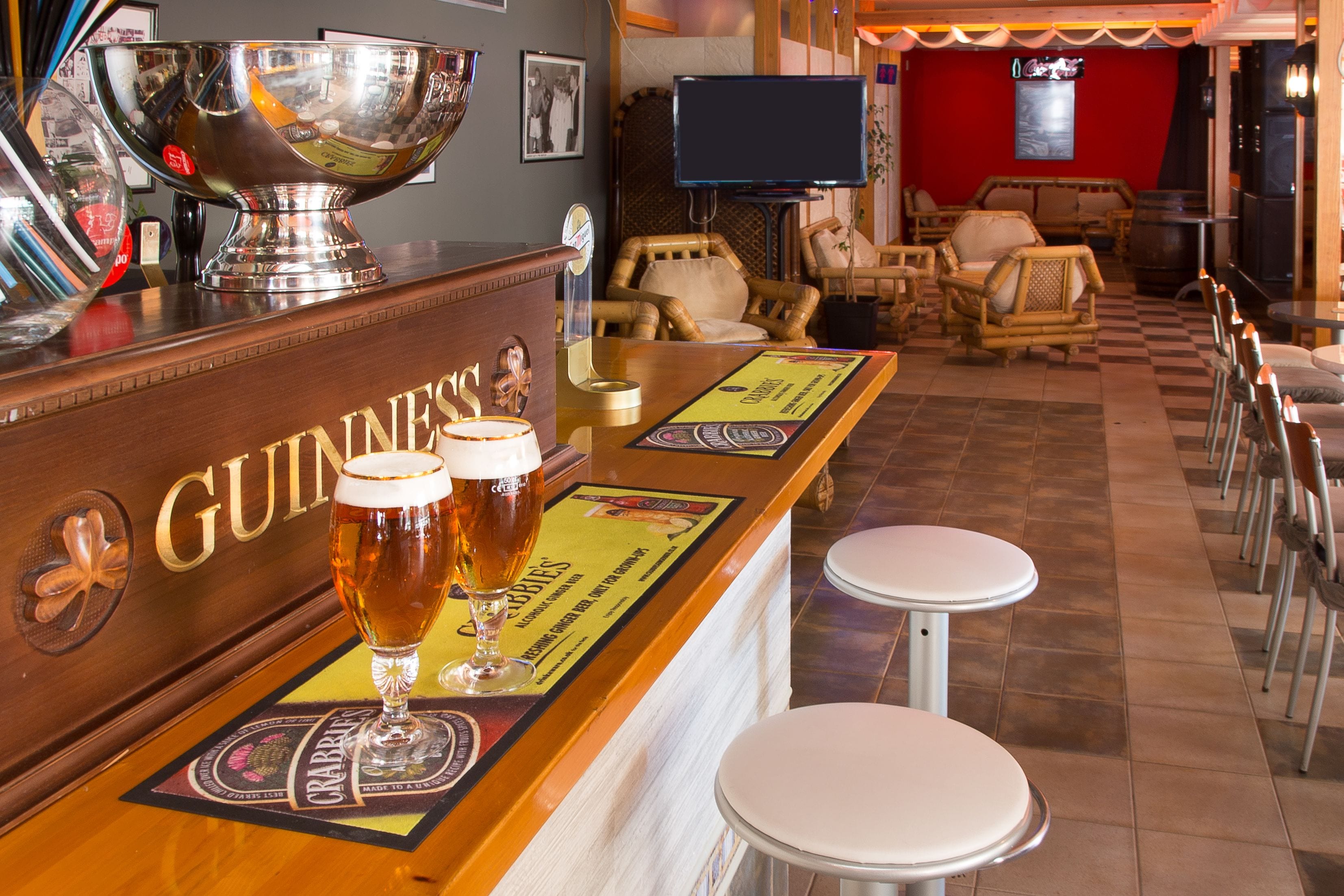 A bar area with Guinness branding, two glasses of beer, and a large silver bowl.