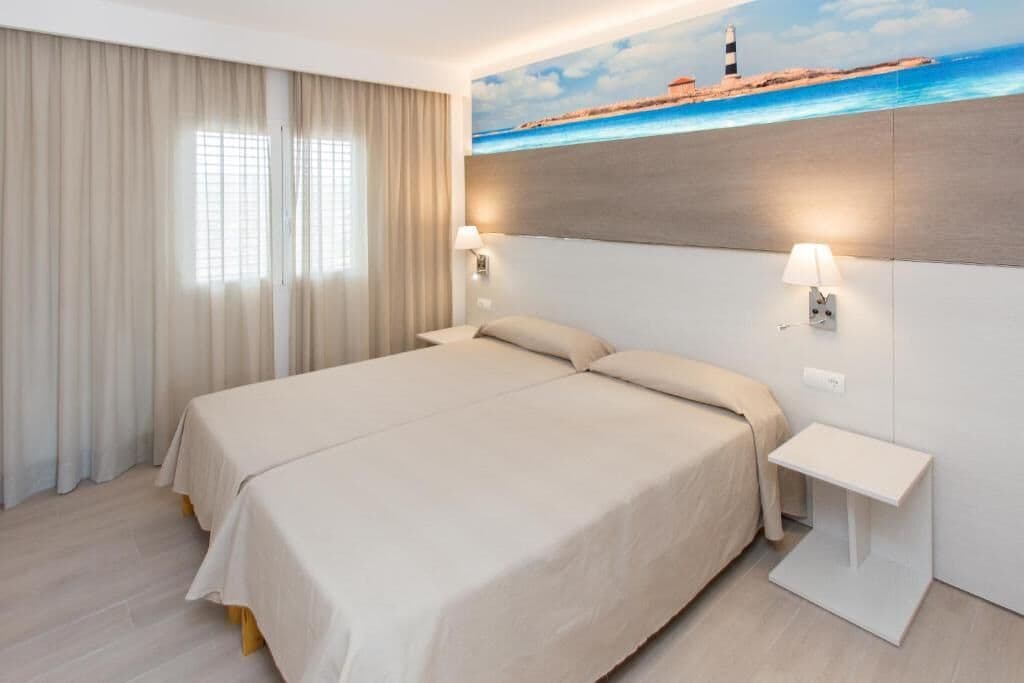 Una habitación de hotel con una cama, dos lámparas de noche, una mesita de noche y un cuadro de un faro en la pared.