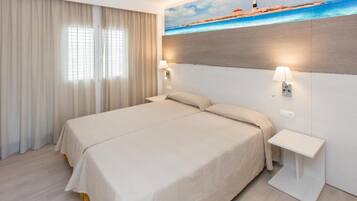 Una habitación de hotel con una cama, dos lámparas de noche, una mesita de noche y un cuadro de un faro en la pared.