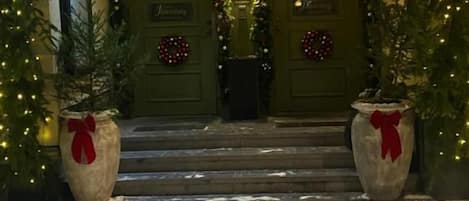 A hotel entrance with a green door, steps leading up to it, and Christmas decorations including lights and wreaths.