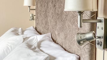 A neatly made bed with white linens, a wall-mounted lamp, and a textured wall design.