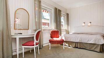 A hotel room with a bed, a desk, a chair, a mirror, and a window with curtains.
