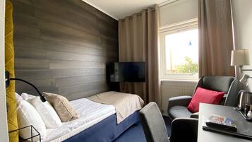 A hotel room with a bed, a desk with a chair, a TV, and a window with curtains.